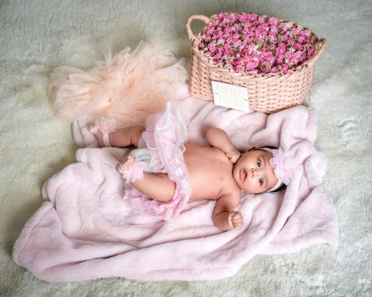 Baby on blanket and wearing tutu beside basket of flowers.