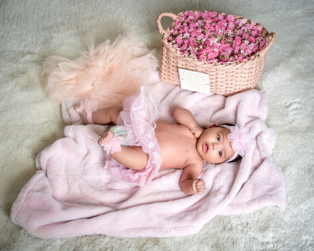 baby on a pick furry blanket by a basket of flowers.