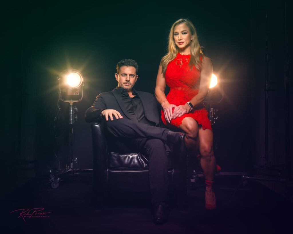 Man and woman seated and posing for photo with stage light behind them.