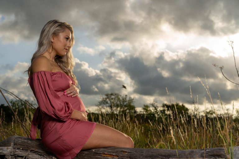 Maternity photo of girl sitting on a log outside.
