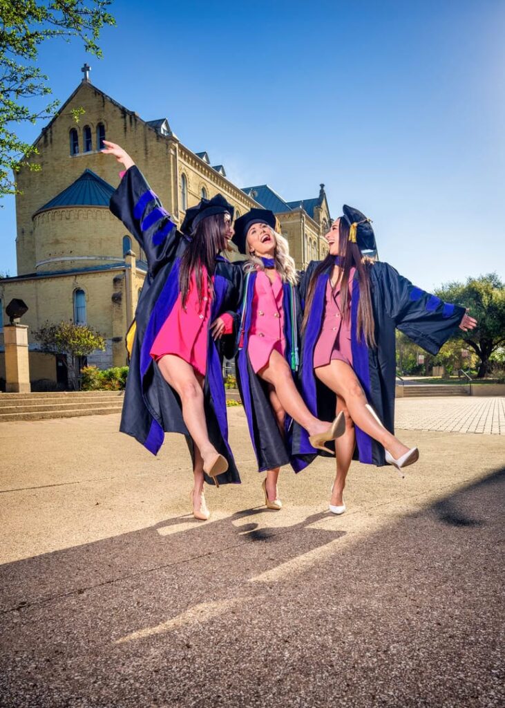 Girls in caps and gowns celebrating on campus in San Antonio at St. Mary's.