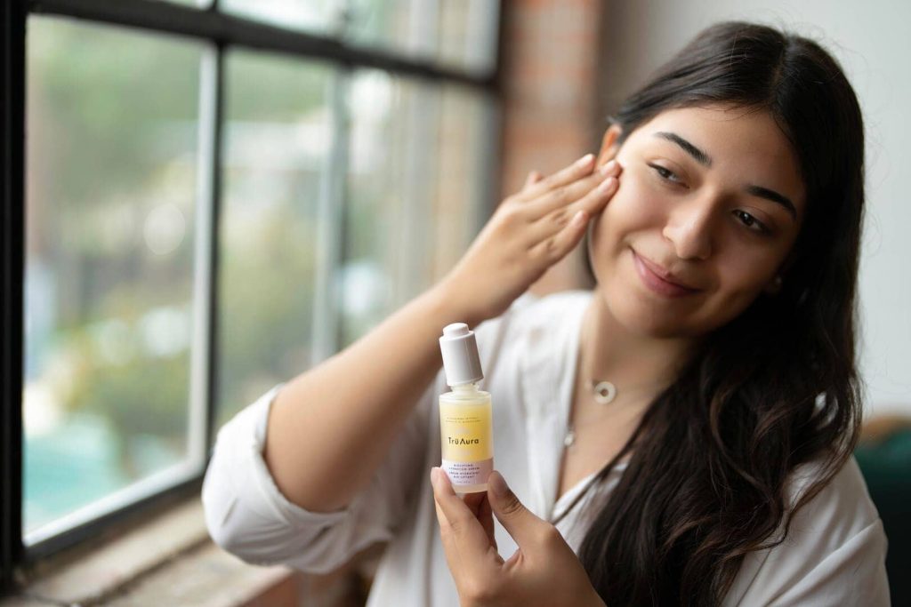 Girl applying skin serum to cheek.