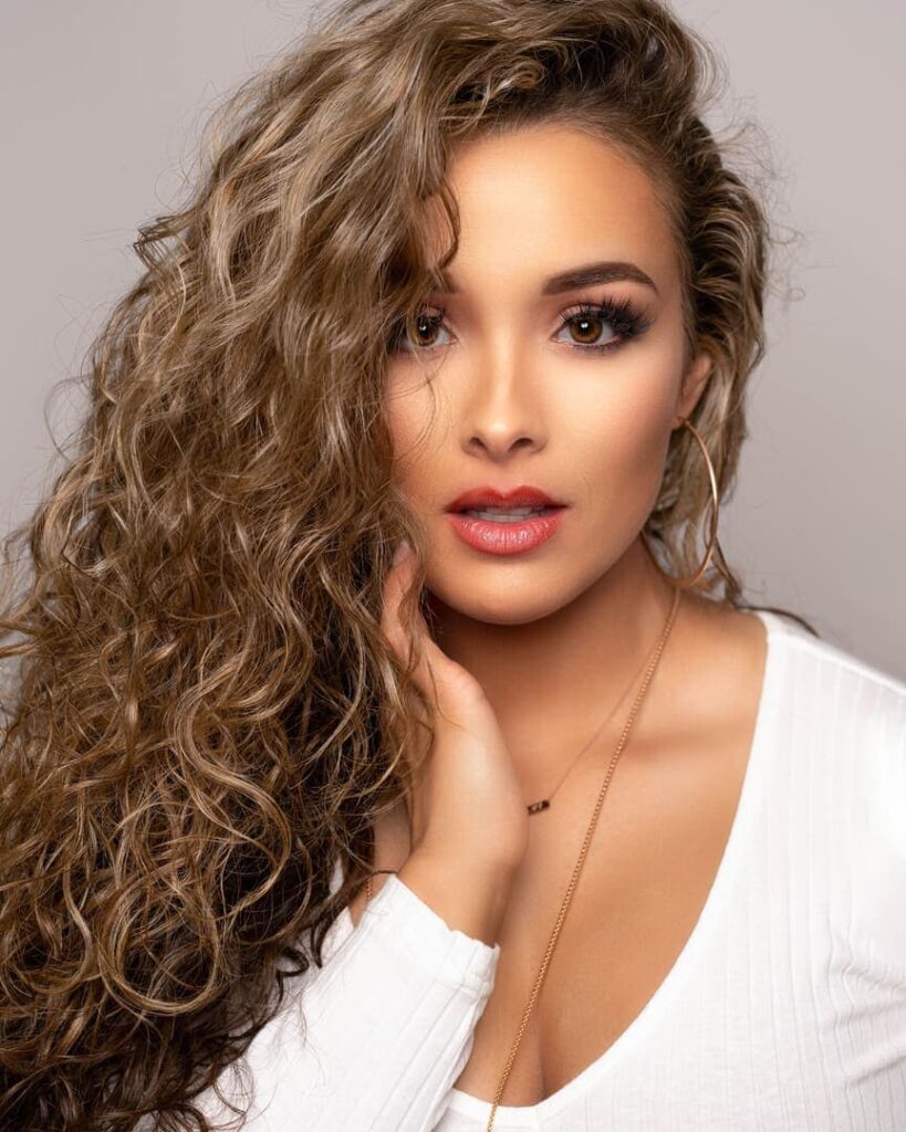 Portrait photograph of a pretty woman with wavy hair and brown eyes.