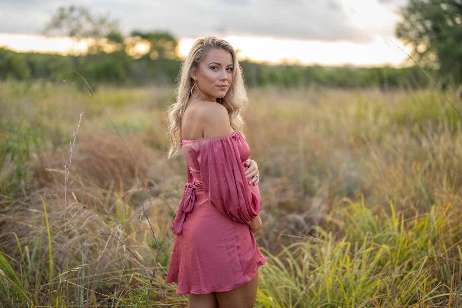 Woman in field posing for maternity photo.