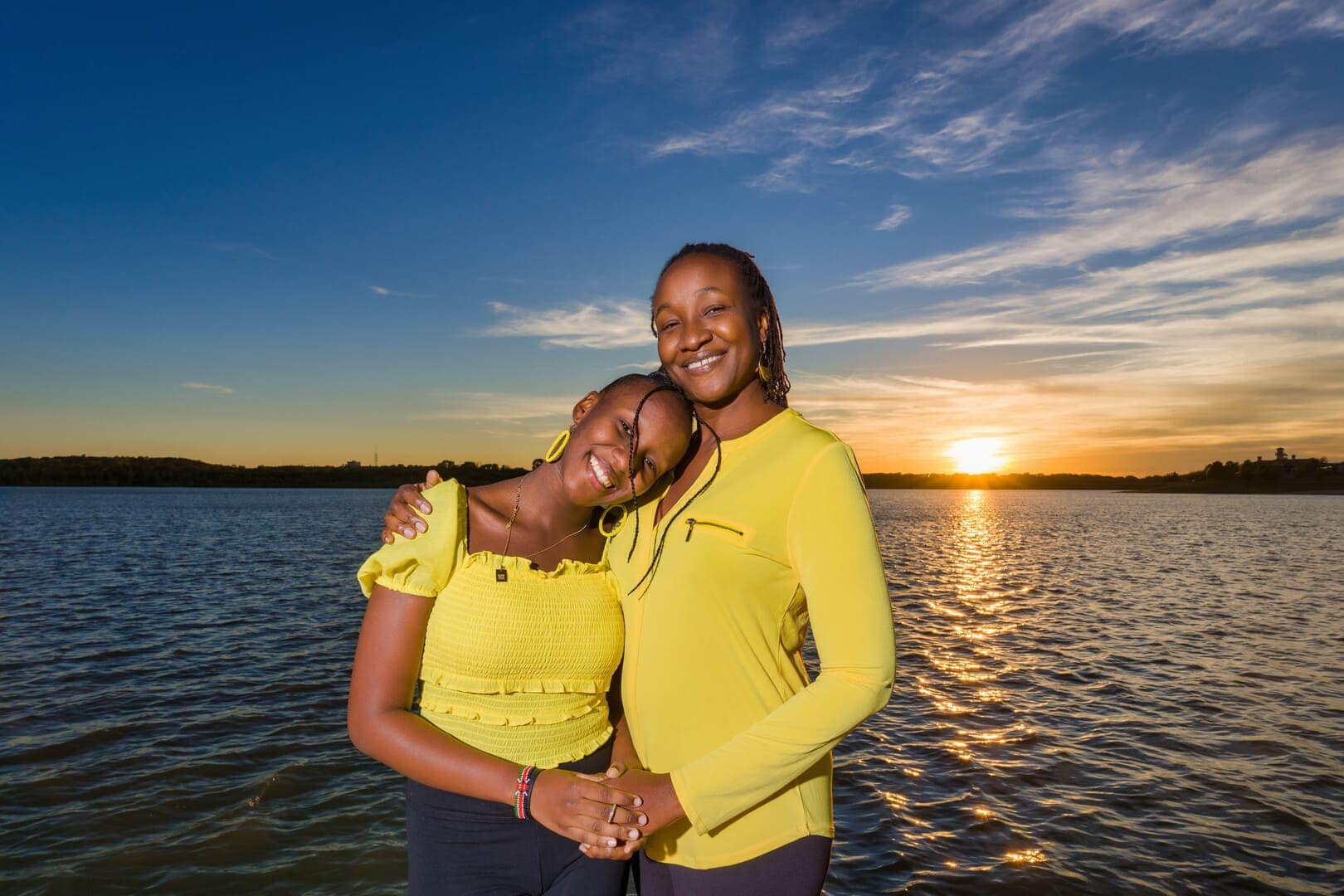 Mother and daughter at sunset by lake.