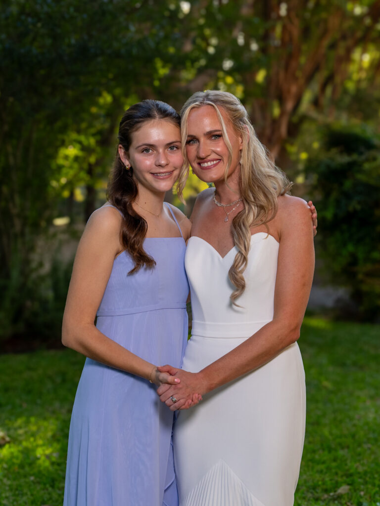 Bride and bridesmaid embrace for photo in a garden.