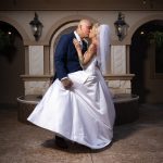 Bride and groom kissing in front of a fountain in a courtyard.