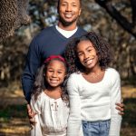 A father and daughters posing for a photo in the woods.