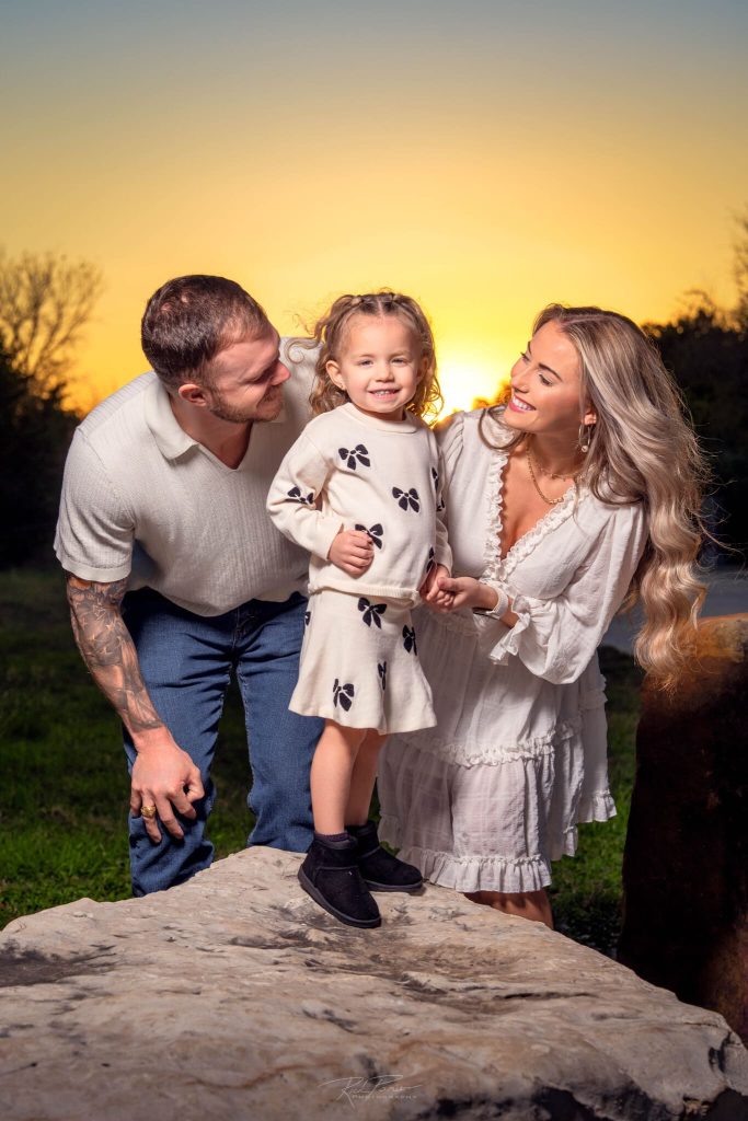 Proud parents looking at child at sunset.